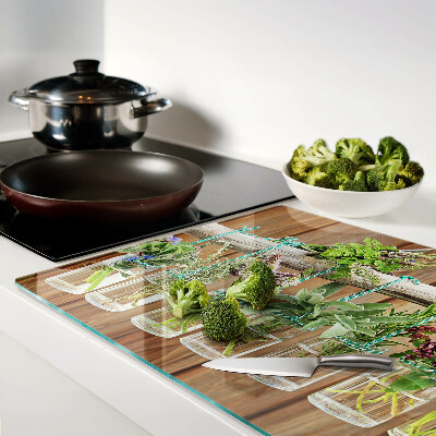 Szklana deska kuchenna z motywem ziół w słoikach na tle drewna